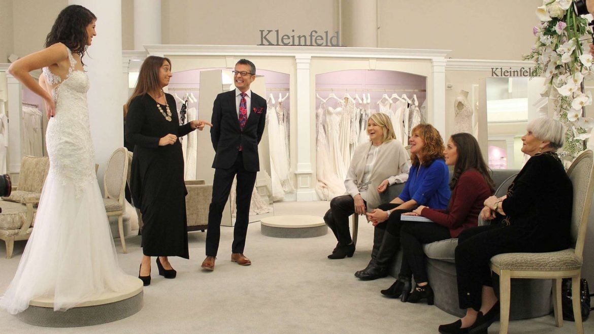 A woman trying on a wedding dress in front of family and friends in a bridal shop.