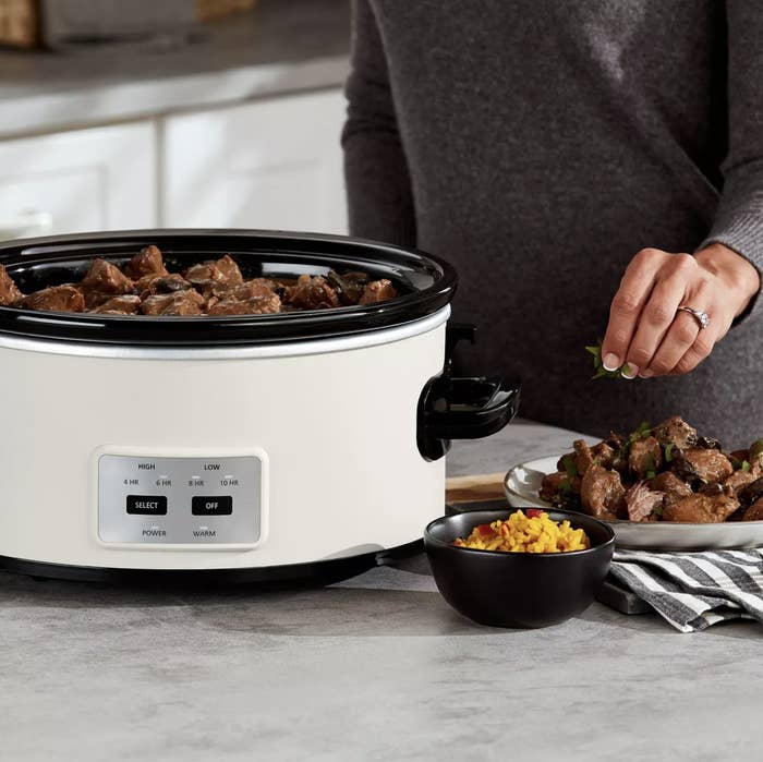 Person is adding seasoning to meat on a dish next to a white slow cooker