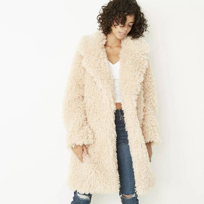 Model is wearing a cream faux fur coat, white tee, and denim jeans
