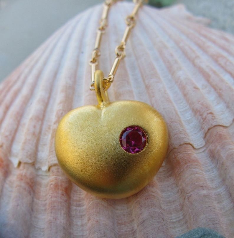 The gold heart shaped pendant with a pinkish-red stone