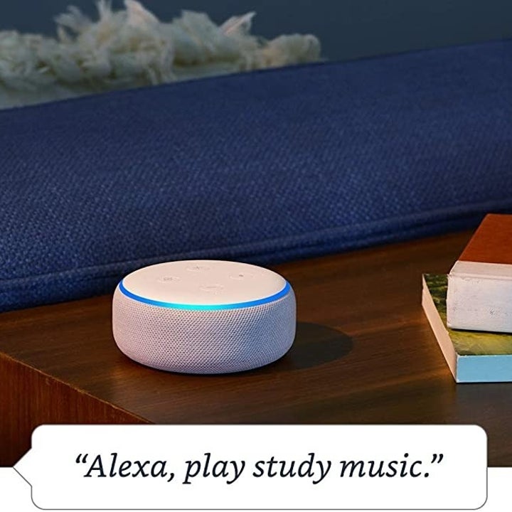 A white Echo Dot with an illuminated blue ring around the top with text that reads "Alexa, play study music" 