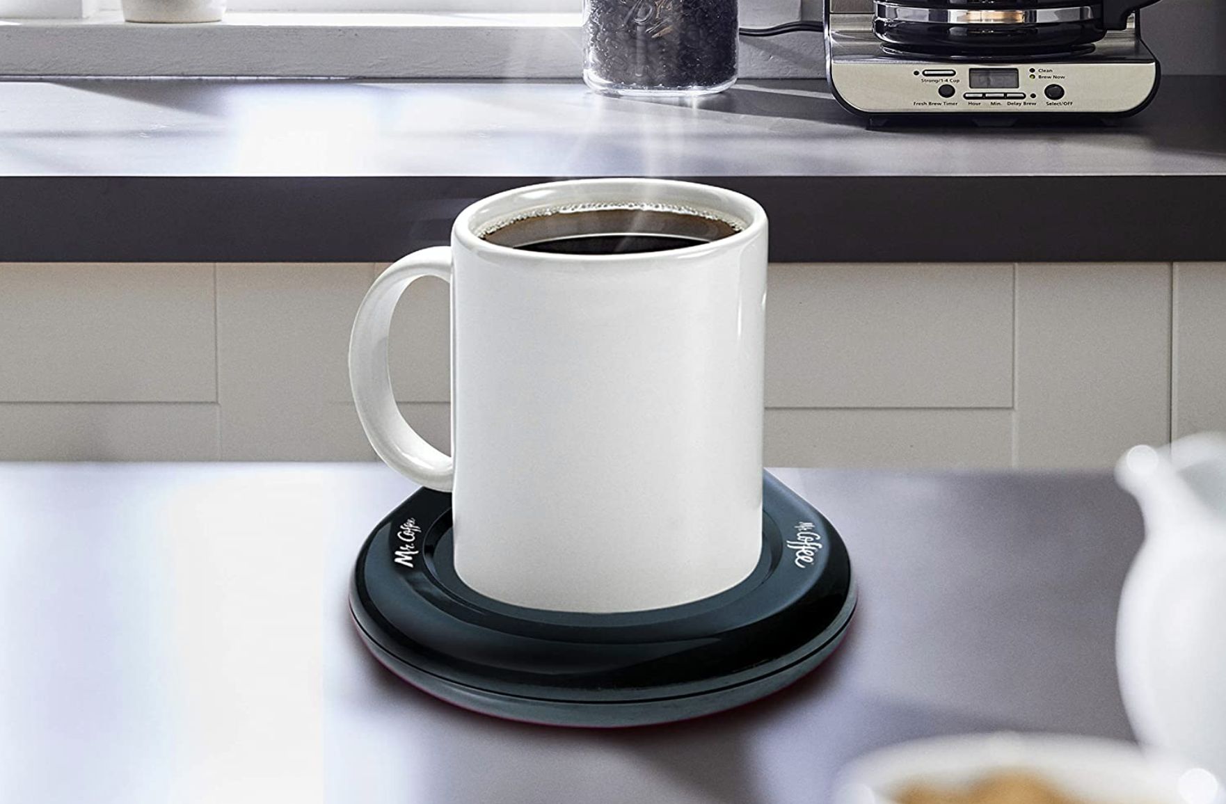 A cup of coffee warmed by a black circular mug warming platform underneath it 