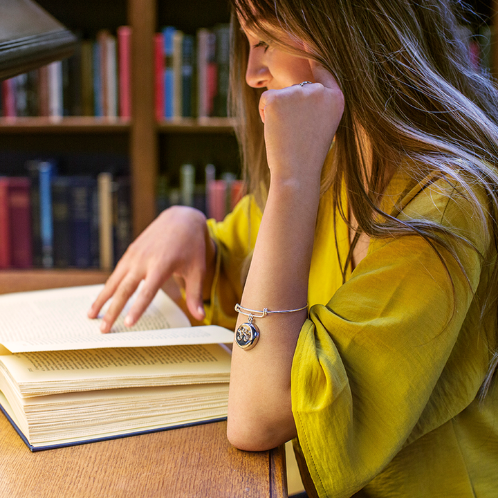 A model wearing an invisaWear bracelet sitting at a desk in a library reading a book 