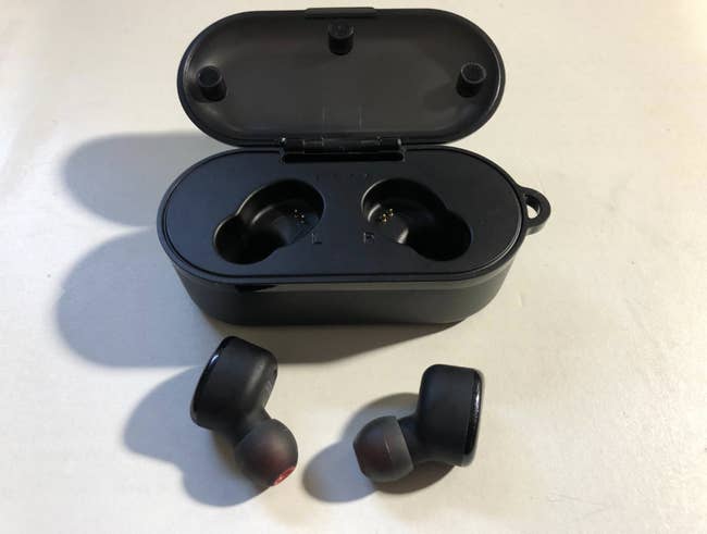 Reviewer's two black earbuds next to their charging case 
