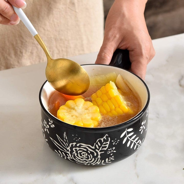 Hand stirs veggie soup in a black-and-white floral soup crock