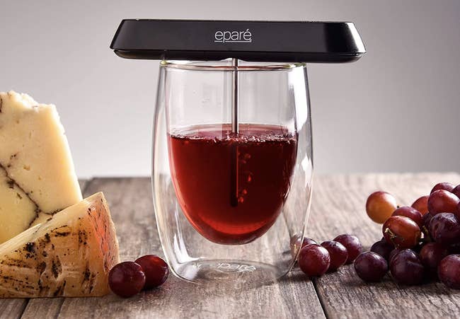 A small black device resting on a glass of wine with a metal tube in it, aerating the wine 