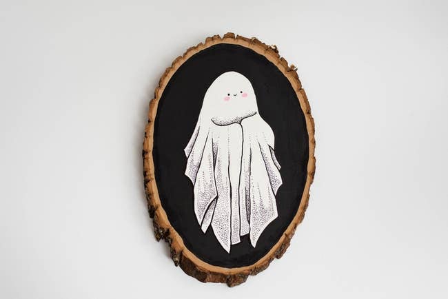 Oval wood piece with painted smiling ghost who has blushing cheeks