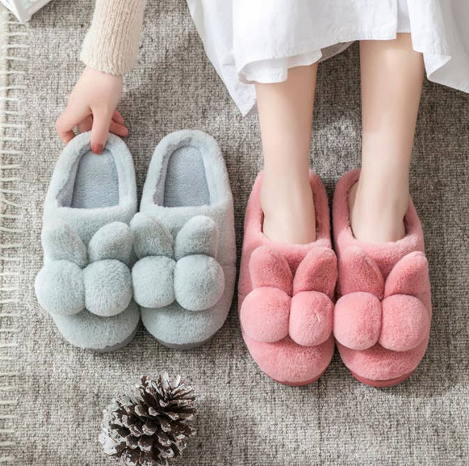 A person wearing the bunny-shaped slippers while sitting next to a pair in a different colour