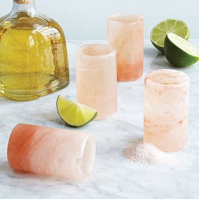 four pink shot glasses next to limes and tequila  
