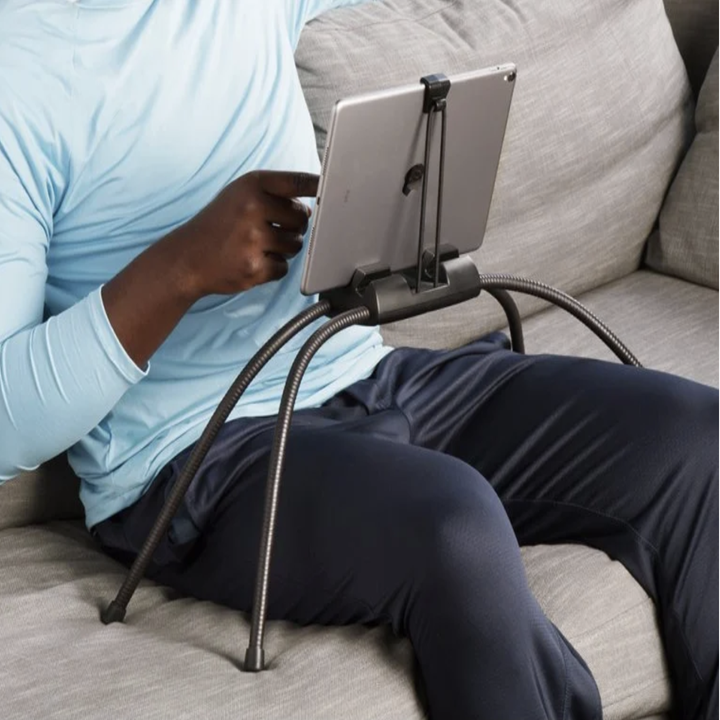 A model using the four legged flexible black stand on a couch with their tablet hovering above their lap 