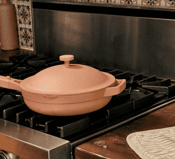 A hand lifting the lid off the spice-colored pan, pulling out the steam basket, and placing it on the counter