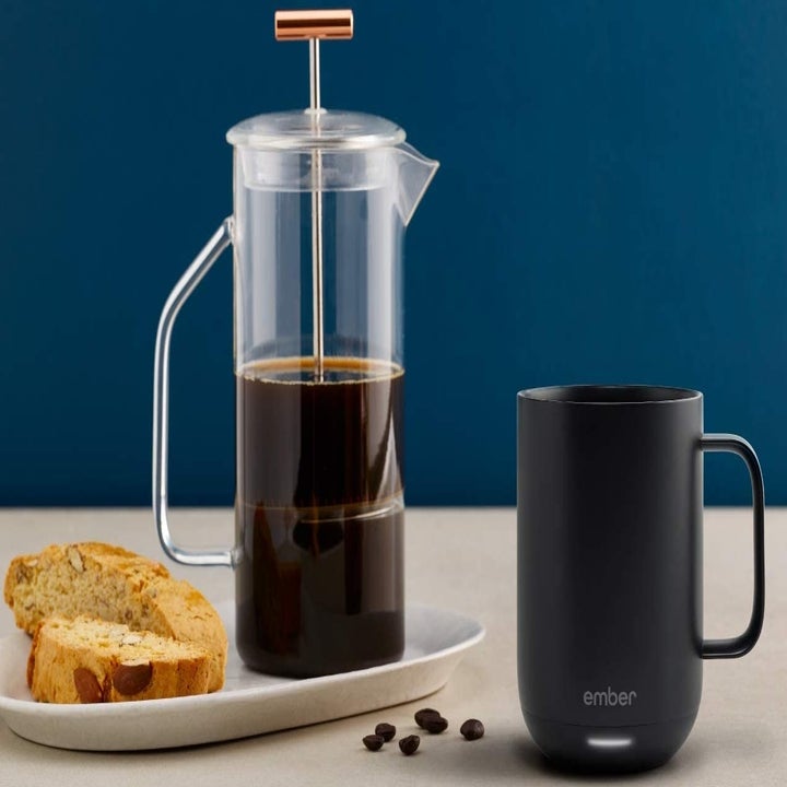 The black Ember mug sitting next  to a French press filled with coffee and a plate of toast 