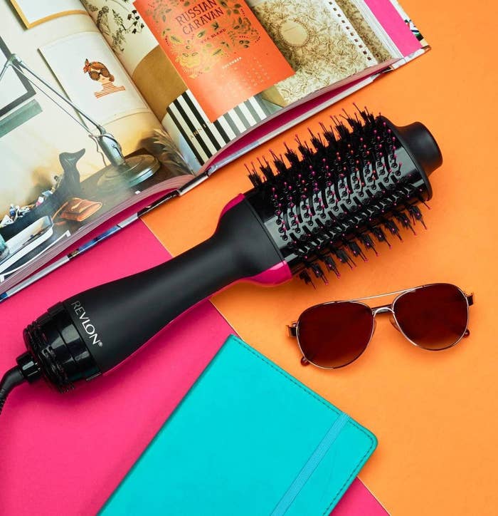 The Revlon hair dryer next to a vibrant magazine, e-reader, and sunglasses to show its size