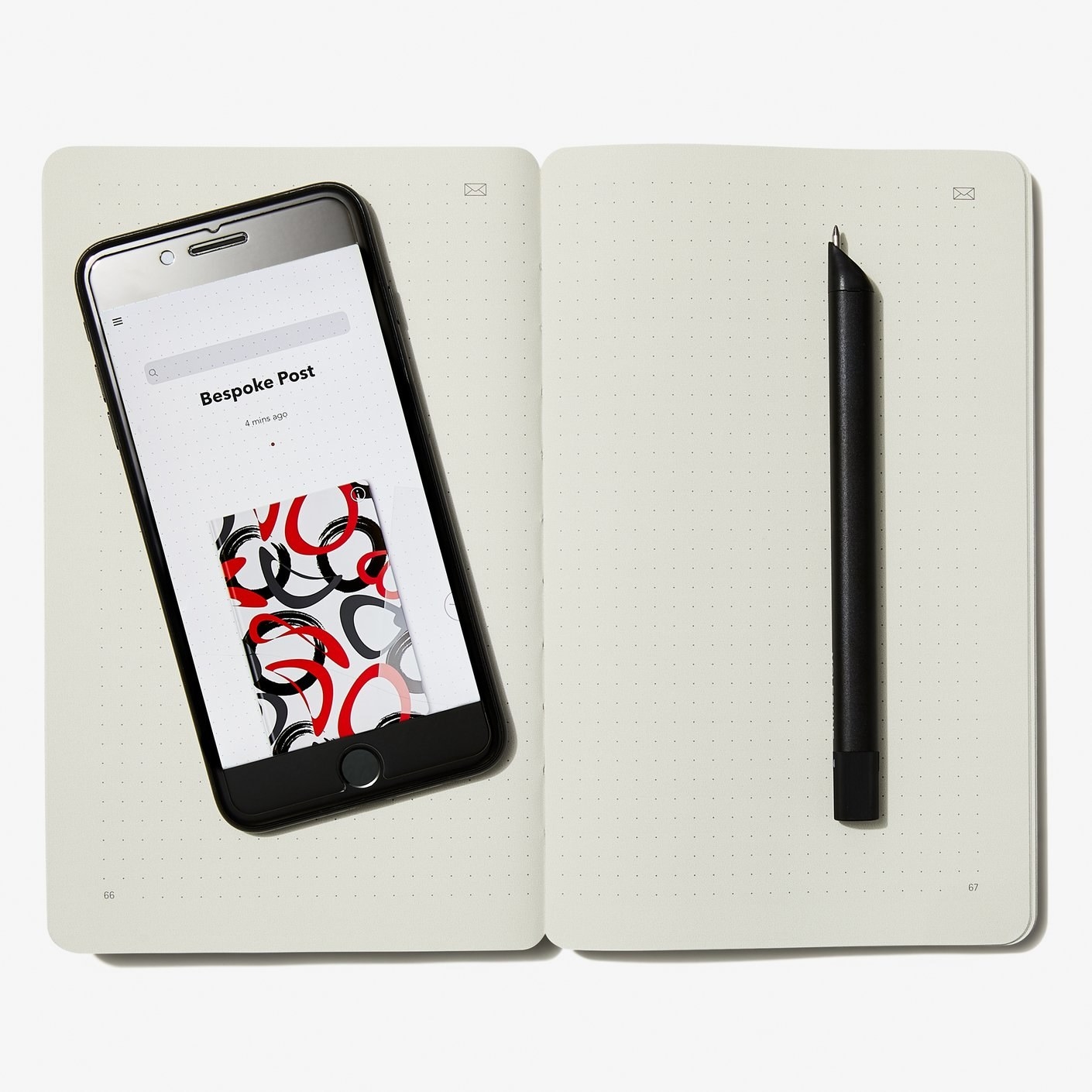 An open notebook with dotted paged, a smartphone with notes pulled up and a Bluetooth-connected pen 