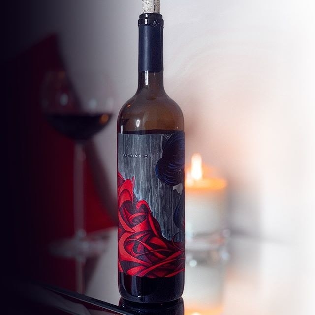 A bottle of wine in front of a tall filled wine glass and a small lit candle