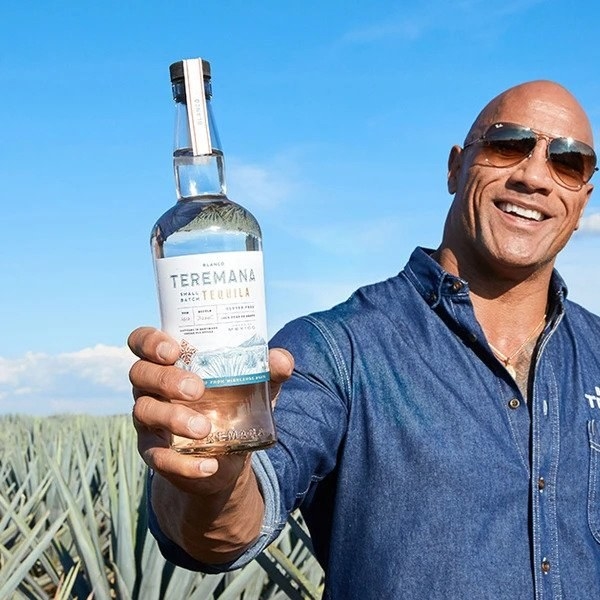 Teremana founder Dwayne The Rock Johnson proudly holding a bottle of tequila in a field in Mexico