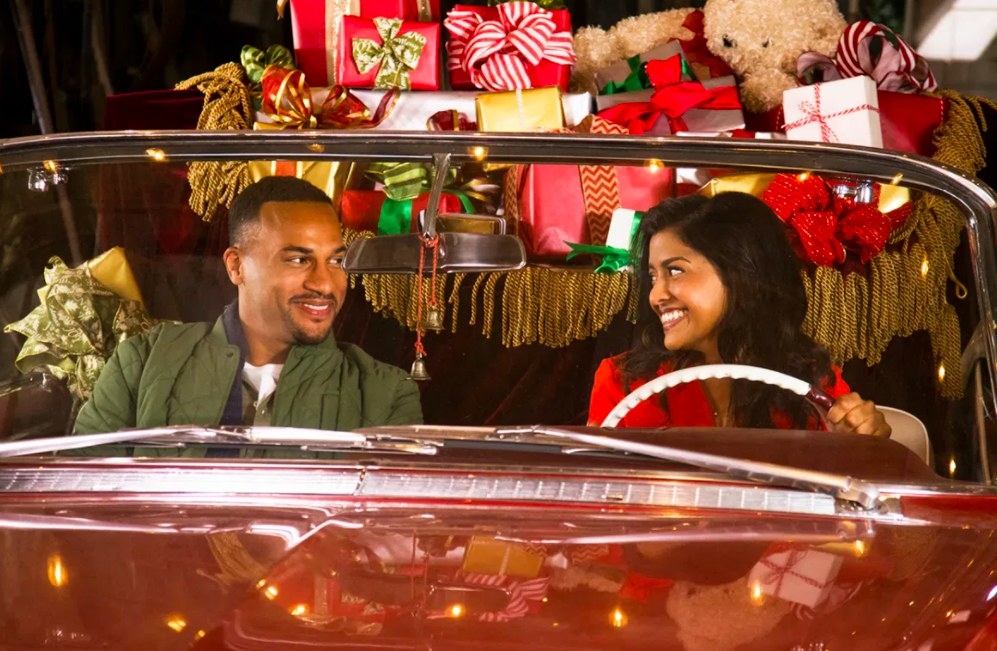 Tiya Sircar and Michael Xavier sit in a convertible car with presents piled up in the back; they&#x27;re looking at each other and smiling
