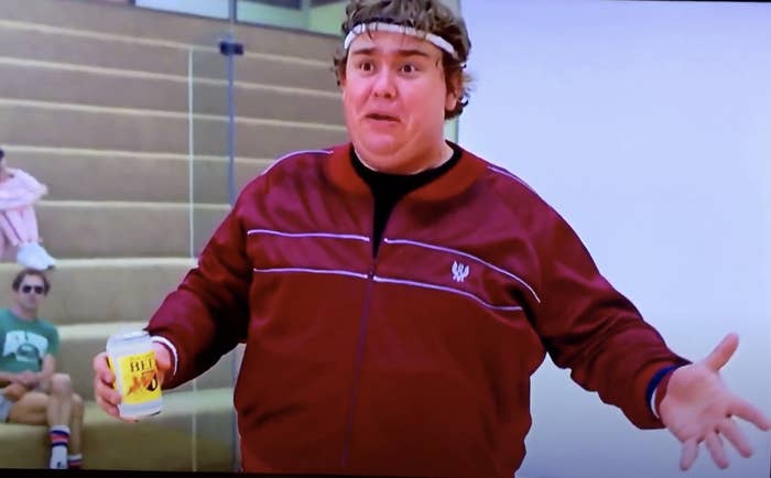 John Candy in workout gear and holding a beer on a racquetball court