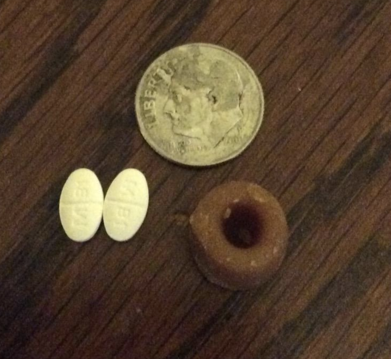 a greenie treat next to two pills and a coin for size