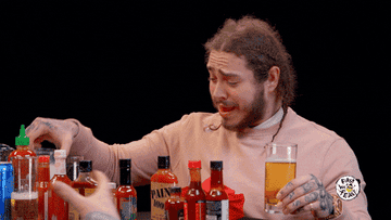 Post Malone reaching for a glass of milk while eating spicy wings