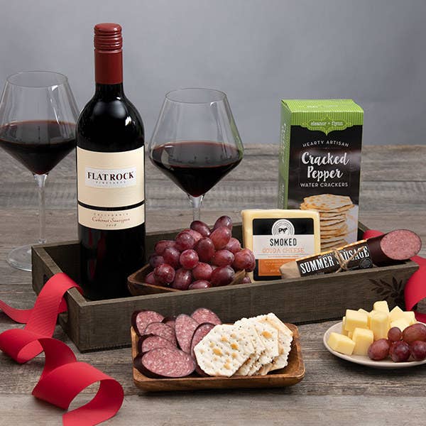 A bottle of wine arranged near an assortments of grapes meats crackers and cheeses