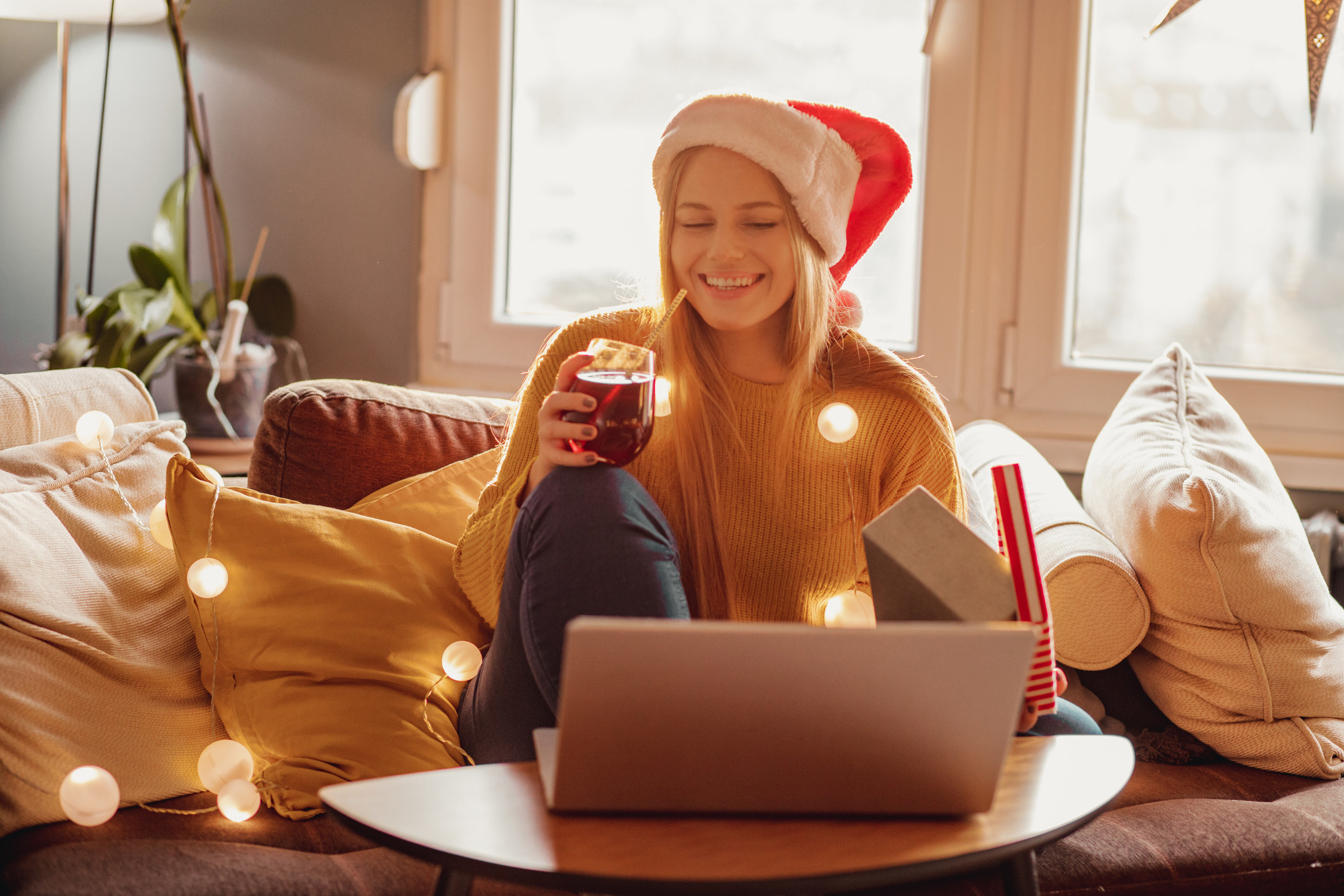 A woman with a Santa hat on, drinking wine and sitting in front of a laptop