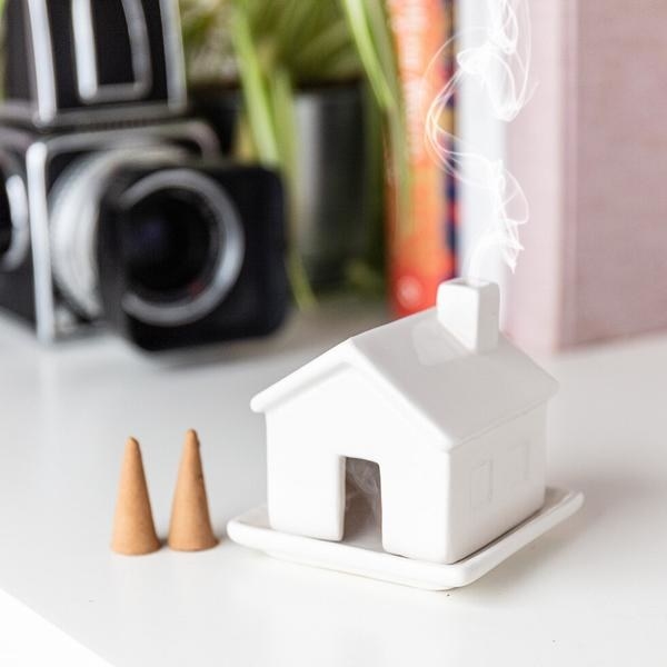 Ceramic house on matching tray with incense inside and smoke coming out of chimney 