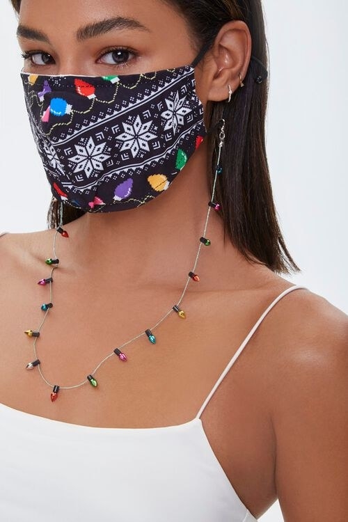 a model wearing the black mask that has white snowflake pattern and colorful lights printed on it with the lights chain