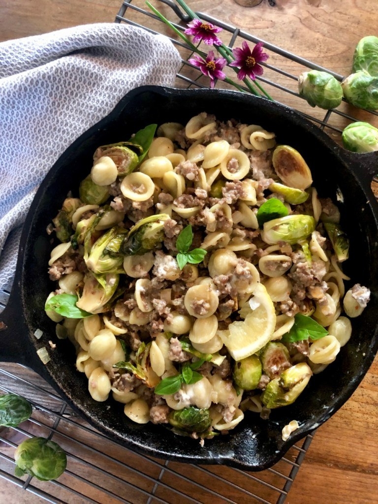 A cast iron skillet with orecchiette, Brussels sprouts, crumbled sausage, and goat cheese.