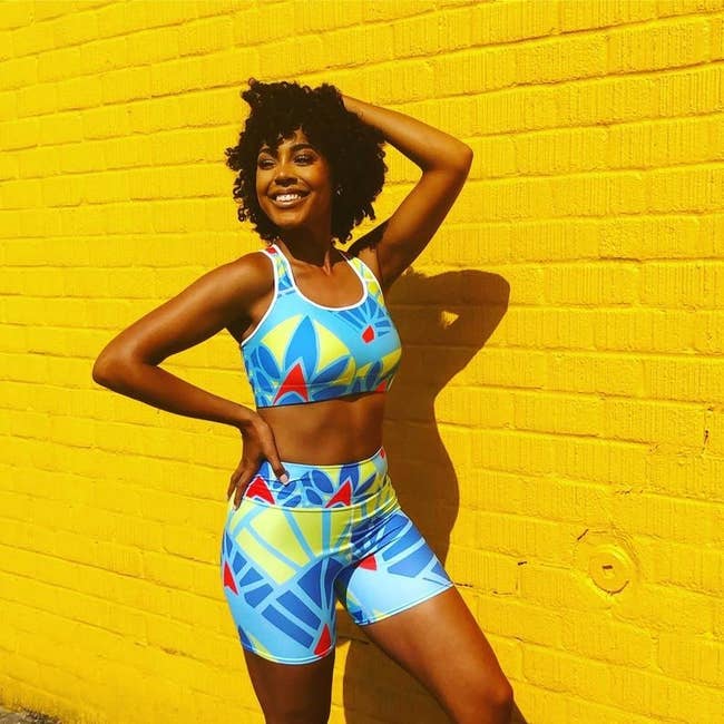 Model wears bright blue, red, yellow, and green-printed high-rise shorts with a matching sports bra