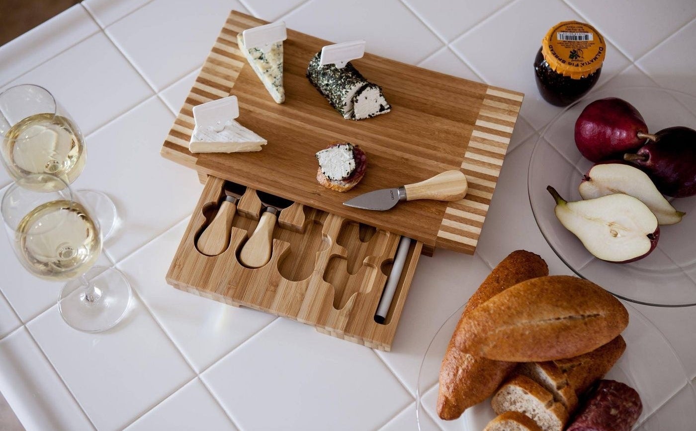 The cheeseboard holding an assortment of cheeses with the drawer open to show its size and the knives