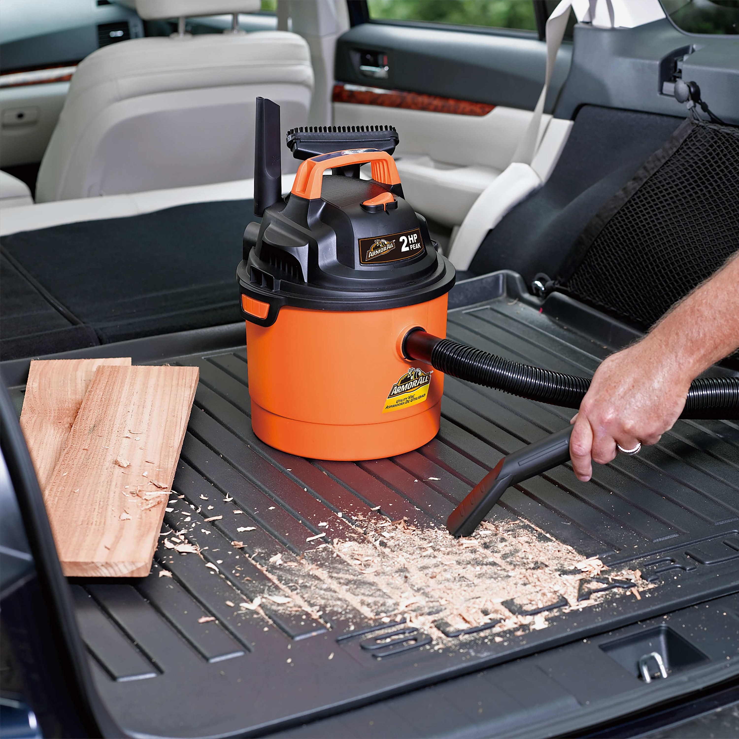 person vacuuming up loose wood chips in their car with a vacuum