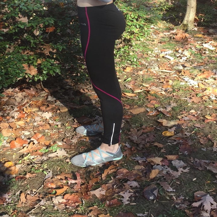 Reviewer wears pair of black leggings with a pink stripe going down the legs and zippers near the ankles
