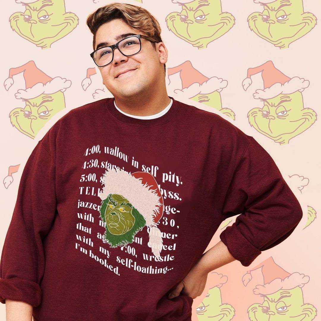 a model wearing a maroon sweatshirt with quotes from the grinch on it