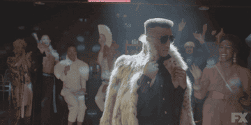 gif of Dyllon Burnside in the TV show &quot;Pose&quot; wearing a fur jacket and turning while walking down a runway with people cheering all around
