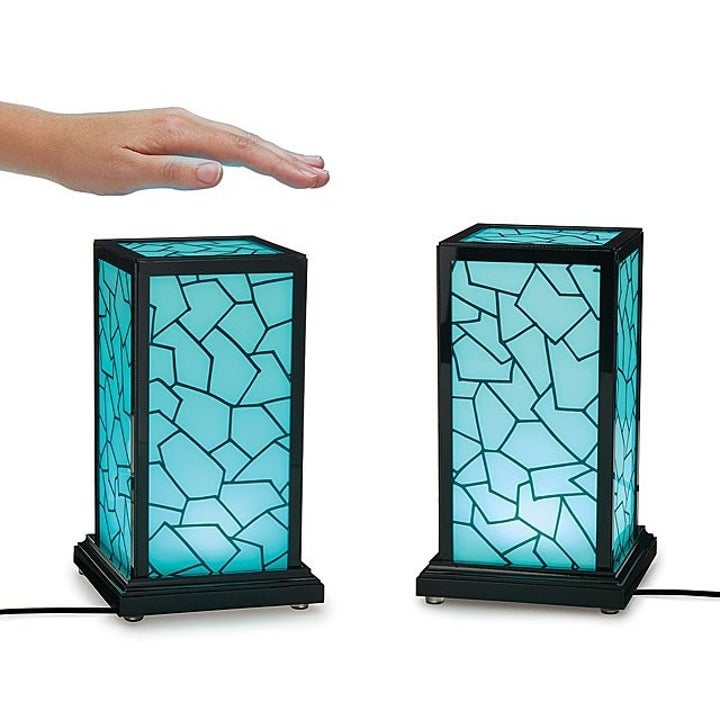 A hand hovering over a pair of blue rectangular column lamps with mosaic-like linework
