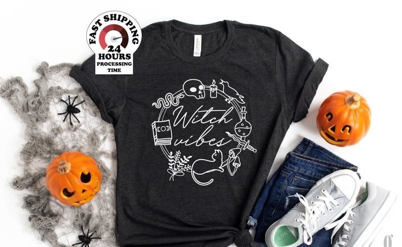 the witch vibes shirt next to halloween decorations, a pair of jeans, and a pair of sneakers
