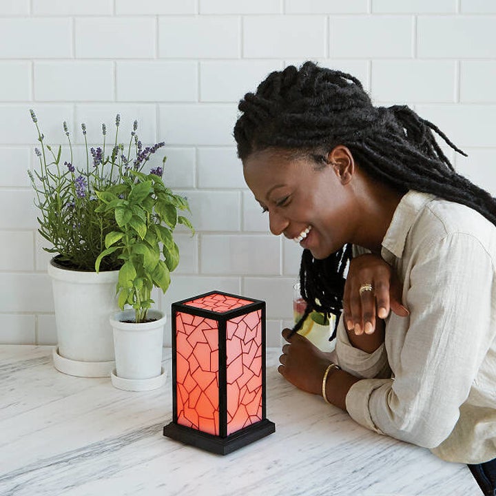 A model smiling at a red rectangular column lamp with mosaic-like linework sitting on a countertop 