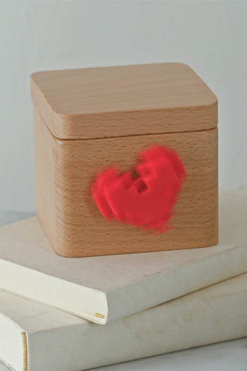 A gif of a wooden box with a three-dimensional heart on the front that is spinning 