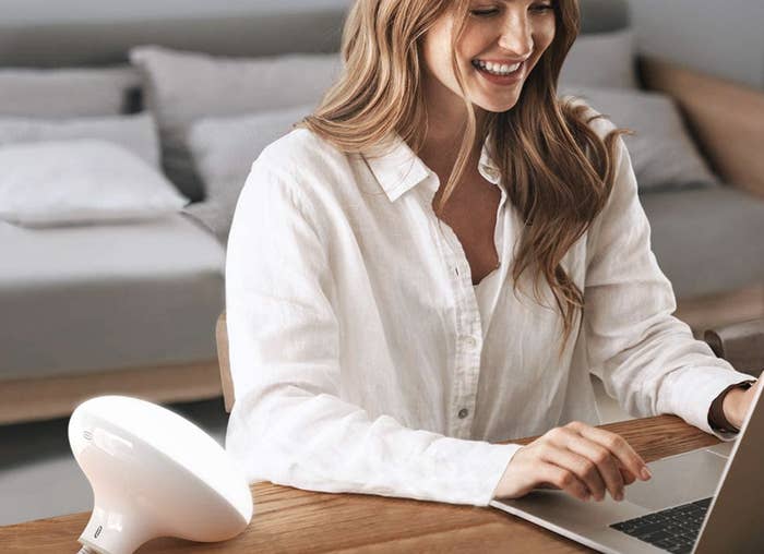 A model sitting next to a round white light therapy lamp propped on a desk 