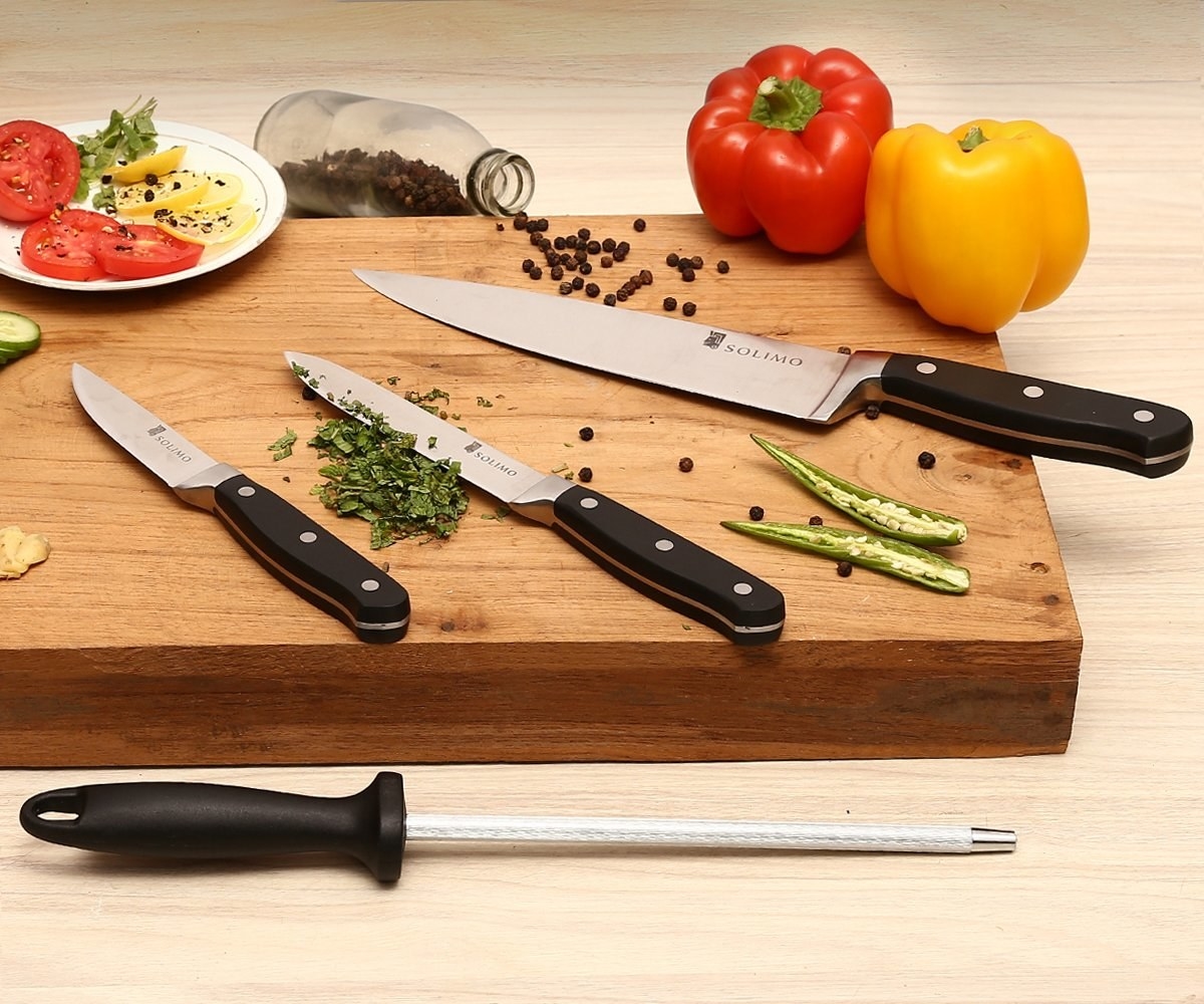 The knife set pictured on a wooden chopping board with chopped veggies and herbs. 