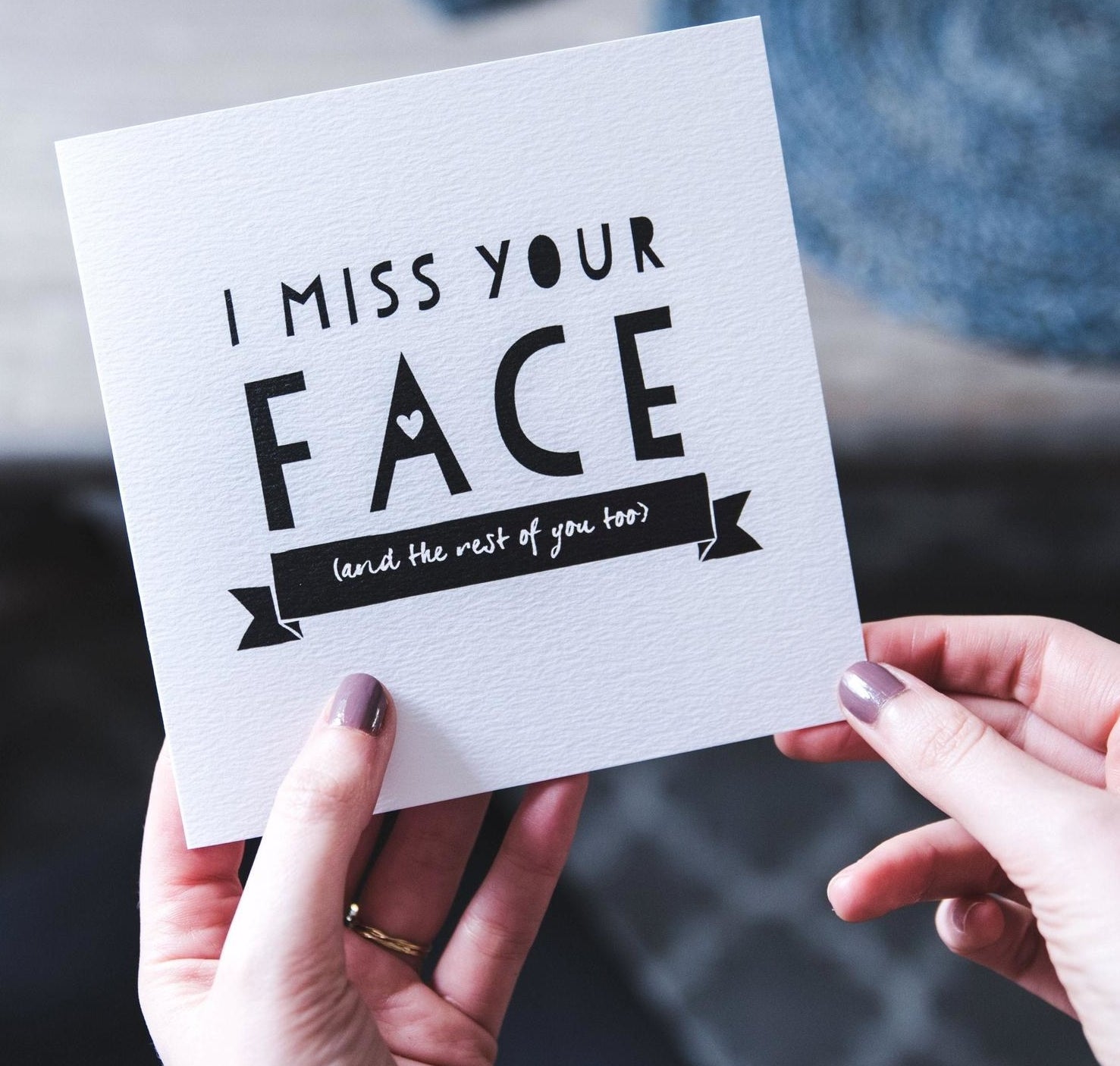Hands holding a white card that reads &quot;I miss your face (and the rest of you too)&quot; in black text 