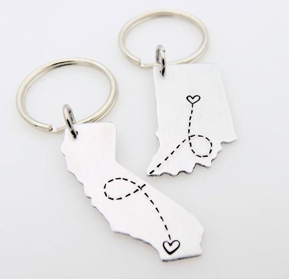 A keychain in the state of California and one in the shape of Indiana with a heart and dotted line etched into each that, when placed side by side, connects the hearts 