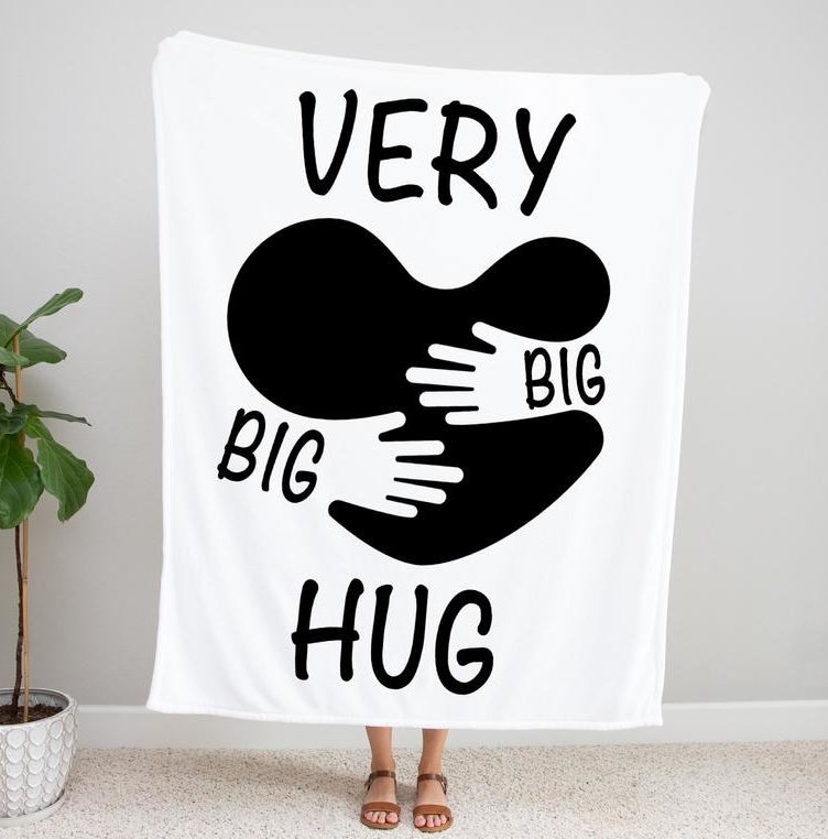 A model holding up a blanket that reads &quot;Very big big hug&quot; with a heart motif being hugged by hands