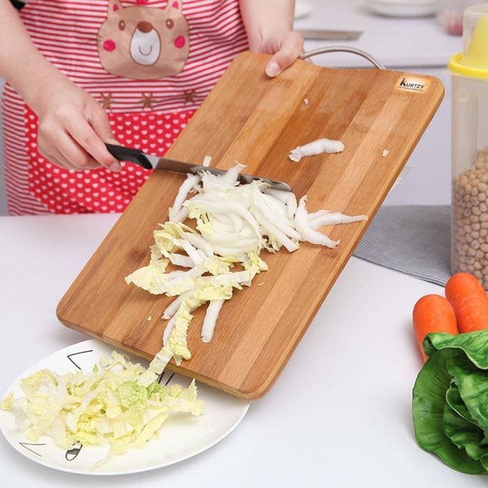 A person transferring chopped cabbage from the board to a plate.