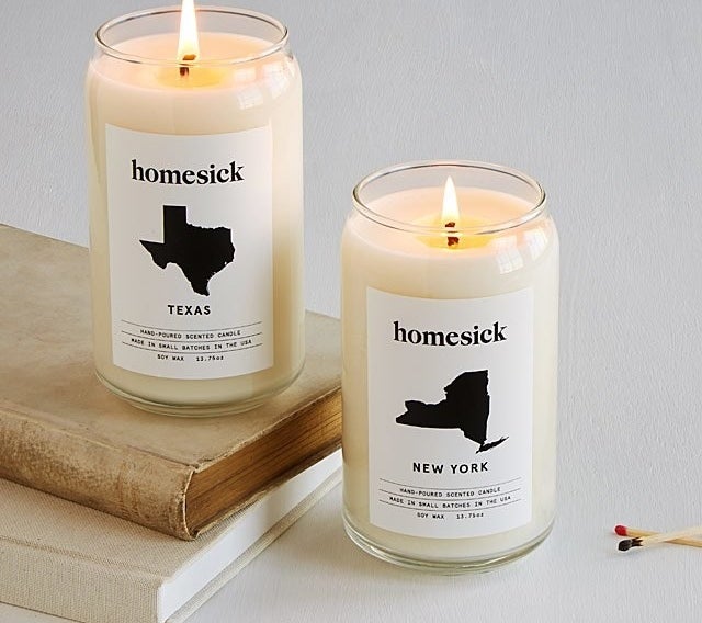 One white Homesick candle with a label featuring an image of the state of Texas and another featuring an image of the state of New York. 
