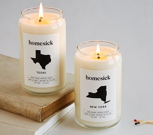 One white Homesick candle with a label featuring an image of the state of Texas and another featuring an image of the state of New York. 