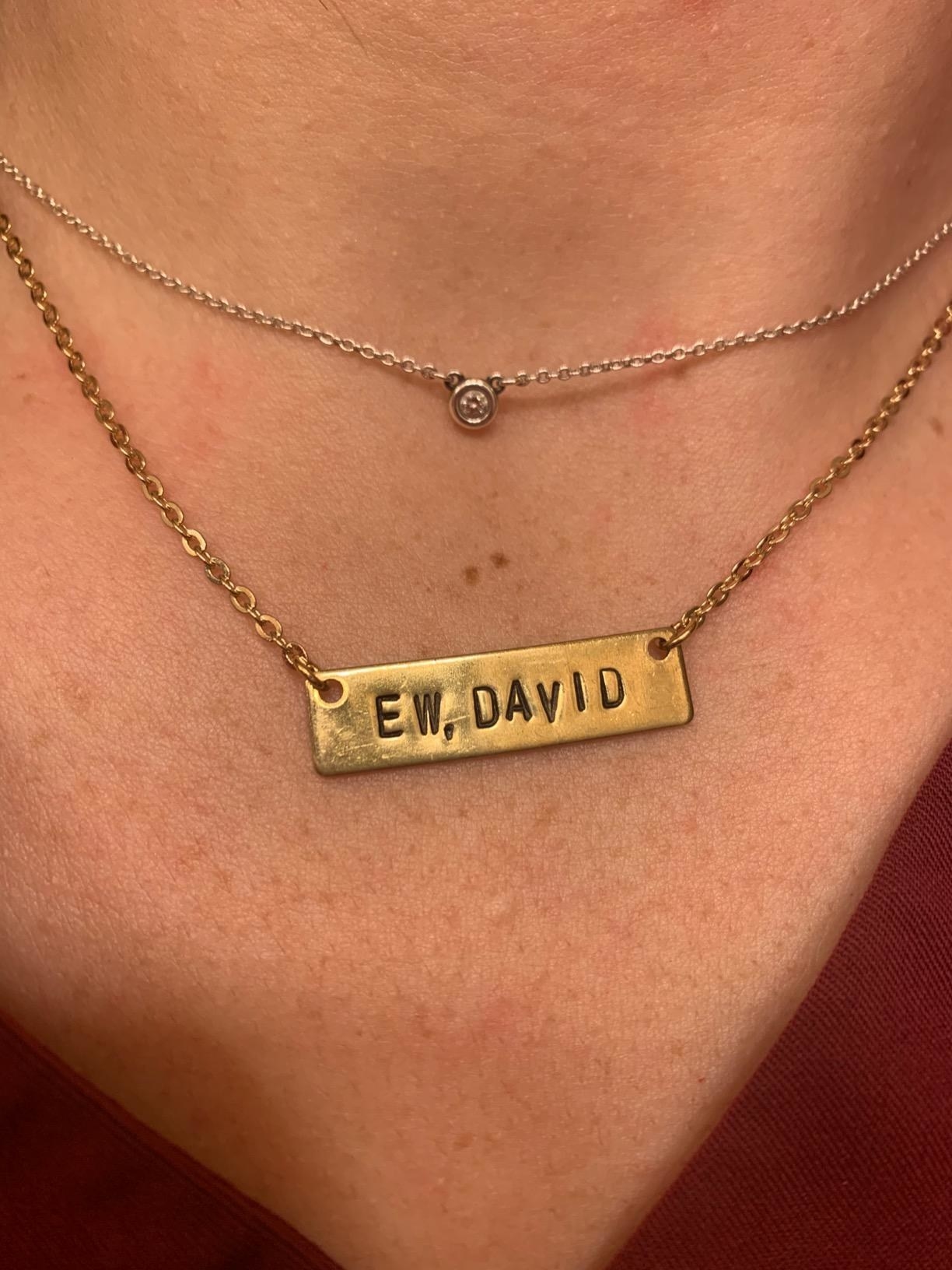 A reviewer wearing the gold rectangular pendant necklace stamped with &quot;Ew, David&quot; layered with another necklace