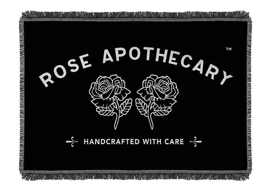 The black fringed blanket with the Rose Apothecary logo that reads &quot;Rose Apothecary Handcrafted with care&quot;
