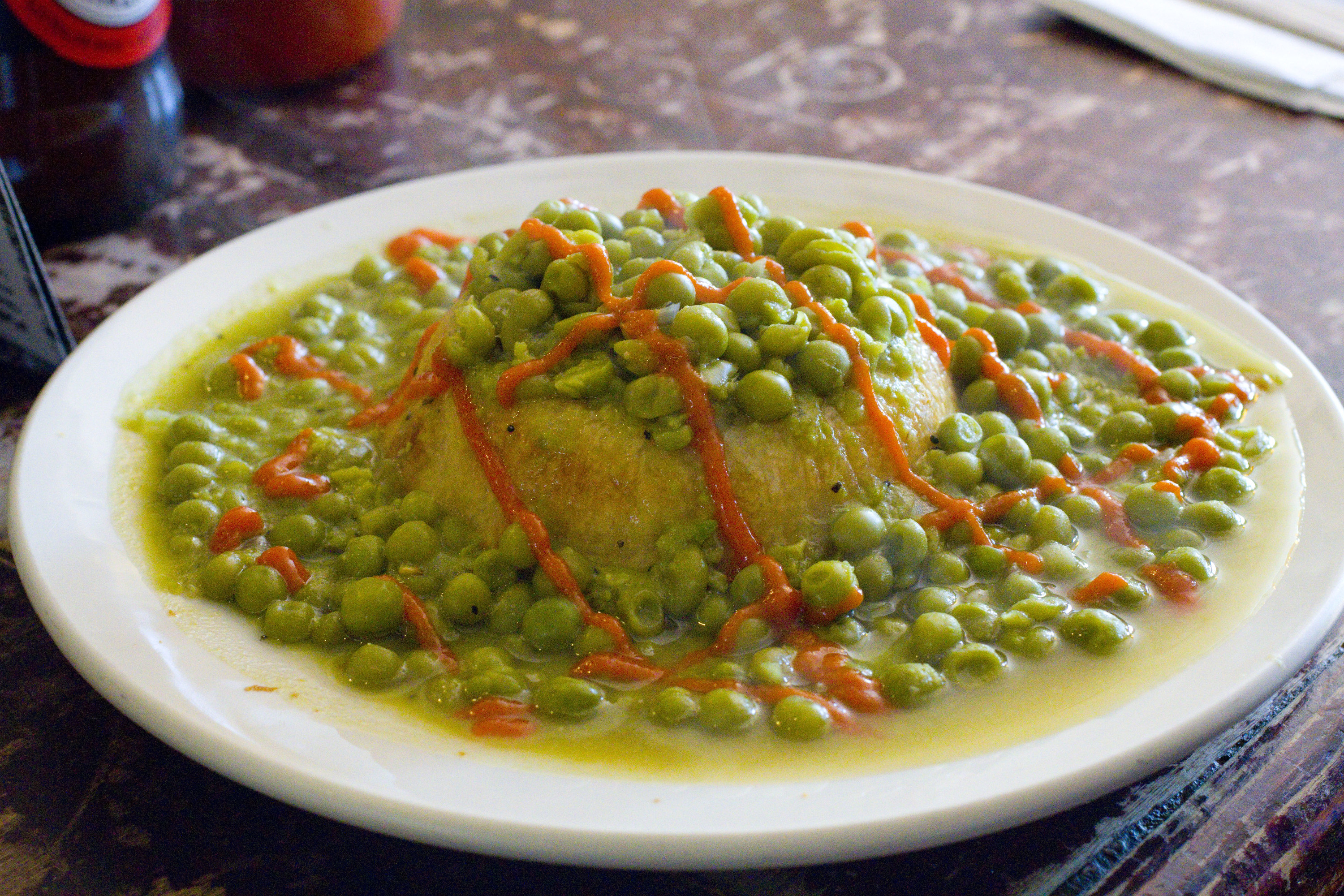 A plate filled with pea soup, an inverted meat pie and a drizzling of tomato sauce